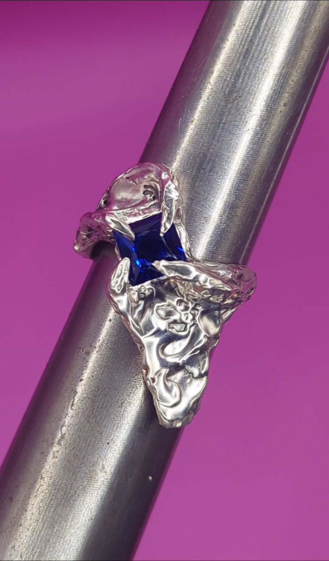 Close-up video of handmade silver ring with sapphire on mandrel – flowing silver texture and deep blue gem
