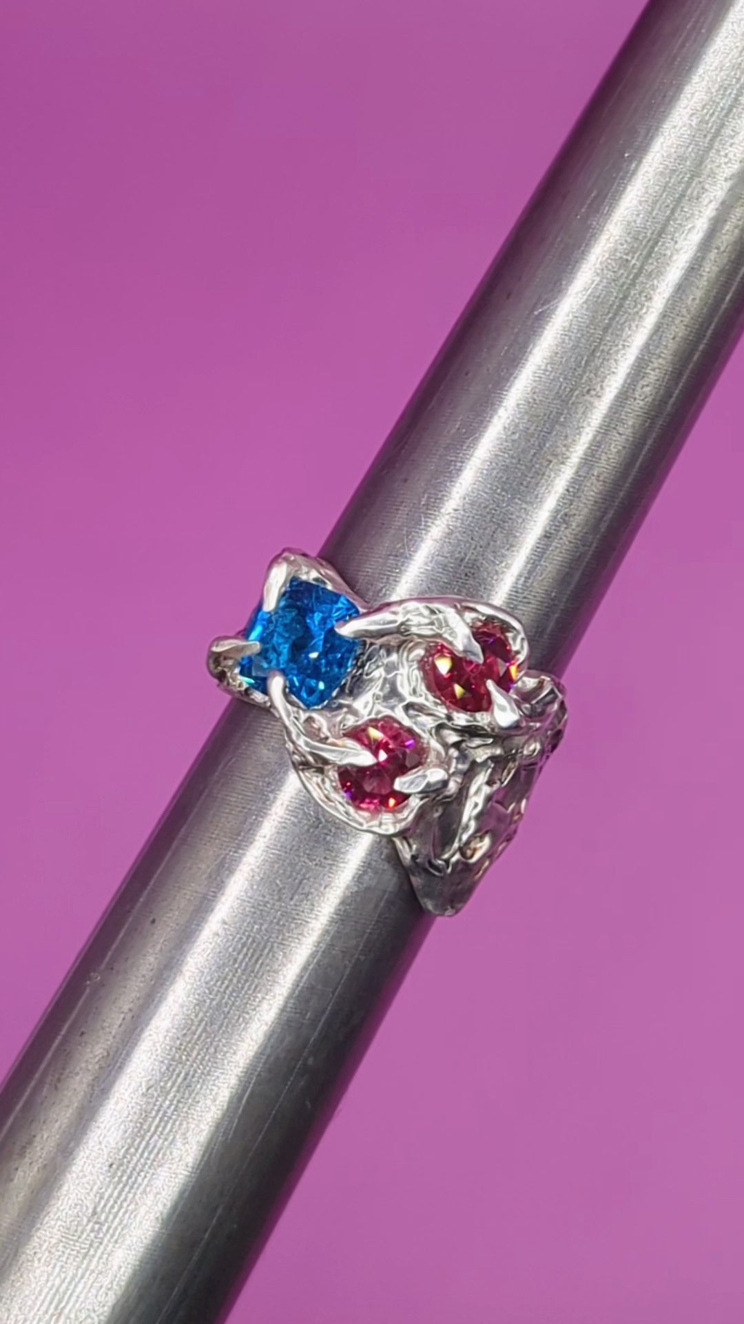 Close-up video of handmade silver ring on mandrel – textured claws with pink and blue nano gems