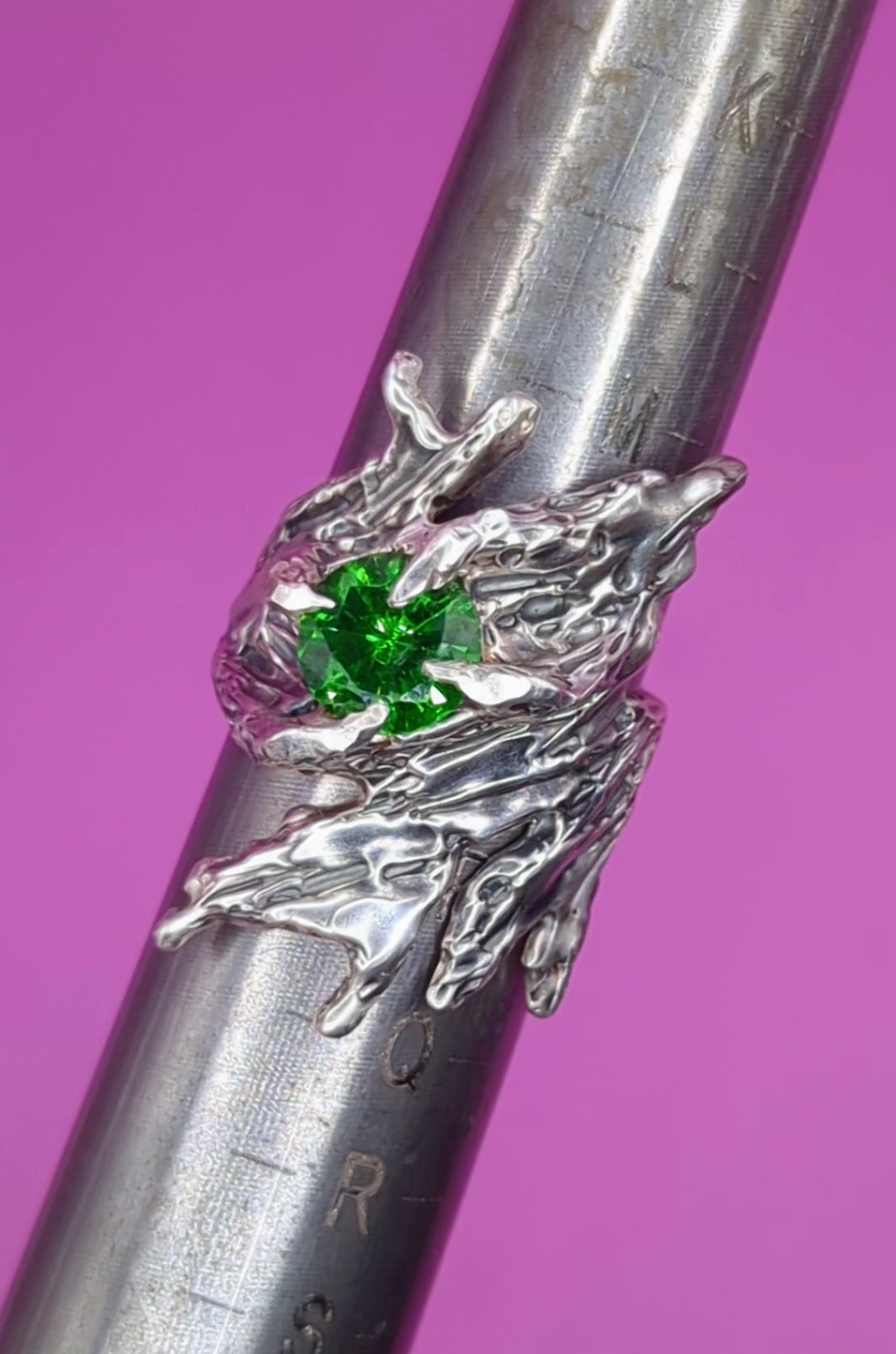 Close-up video of handmade silver ring with green CZ on mandrel – textured band and bold gem